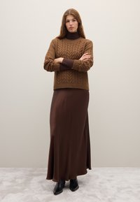 Brown knitted sweater with a textured pattern, paired with a long brown satin skirt and black ankle boots on a light gray carpet.