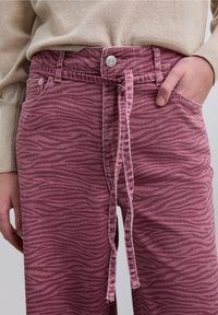 Pantalon imprimé zèbre rose en matière douce et texturée. Doté d'un lien à l'avant, d'une fermeture par bouton et de poches latérales.
