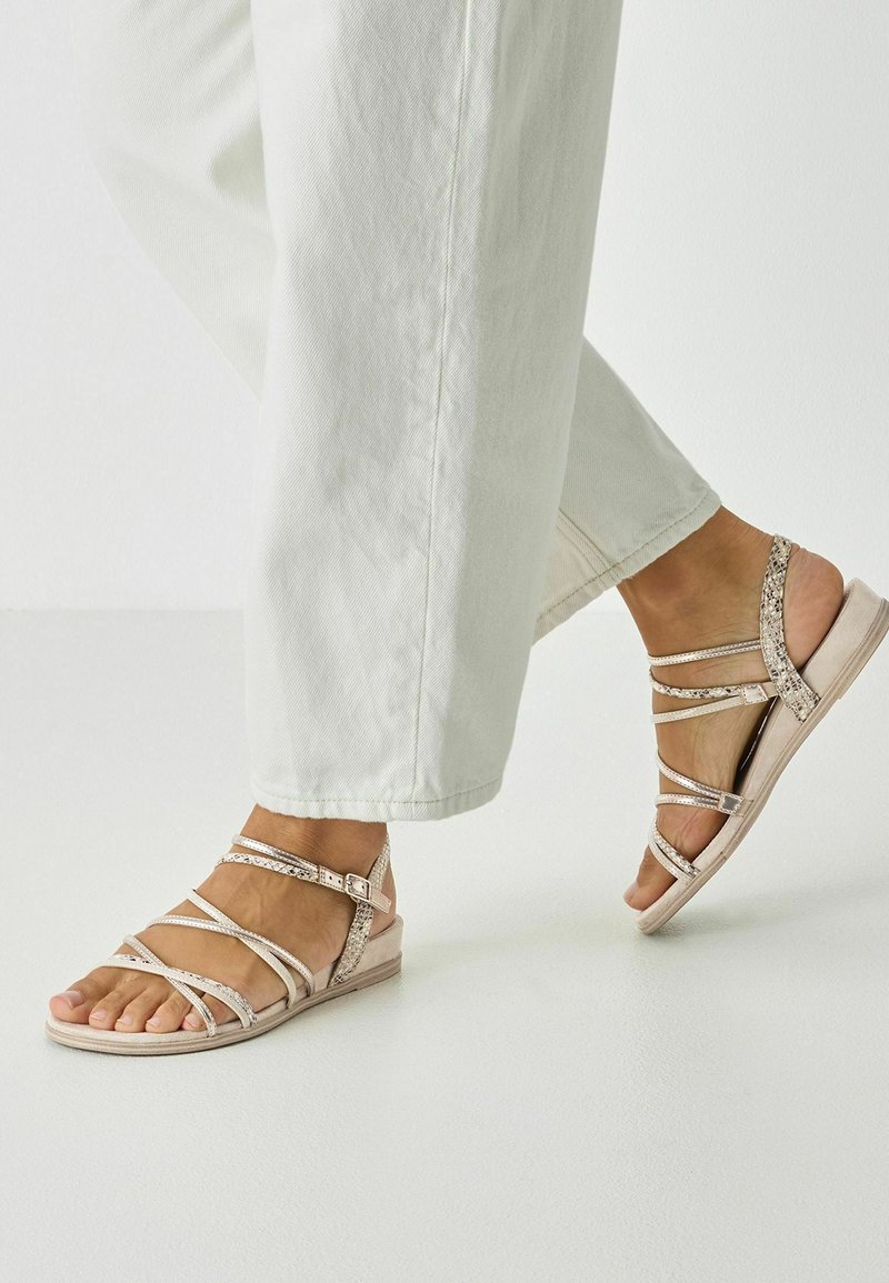 Light pink sandals with multiple thin straps and a textured accent. The heel is low and cushioned, suitable for casual wear.