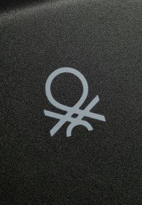 Superficie nera testurizzata con un logo grigio composto da forme circolari e lineari, con una linea orizzontale evidente sotto il cerchio.