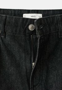 Czarne jeansy z denimu mają zamek błyskawiczny, metalowy guzik i teksturowane wykończenie. Etykieta widoczna wewnątrz pasa.