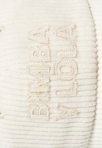 Tejido de pana blanca con acanaladuras verticales, con texto bordado "BIMBA Y LOLA" en un beige claro. Textura suave con un sutil brillo.