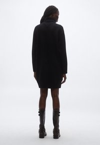 Musta neulemekko korkealla kauluksella, pitkät hihat ja resoripintainen. Yhdistetty polven korkeisiin nahkasaappaisiin, joissa on hihnat.