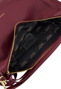 Innenraum einer burgunderroten Ledertasche mit einem Reißverschlussfach und einem dunklen Stofffutter mit goldenen Logomustern. Sichtbare goldene Reißverschlussbeschläge.