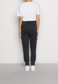 Svarta cargobyxor med elastisk midja och muddar, med sidofickor och bakfickor med dragkedja, kombinerat med en vit t-shirt och vita sneakers.