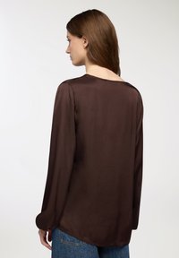 Blusa di seta marrone con maniche lunghe, scollatura ampia e una texture liscia, abbinata a pantaloni in denim azzurro chiaro.