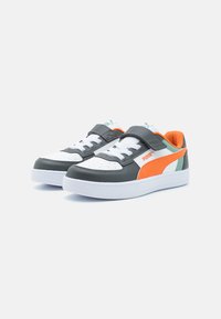 Les baskets Puma possèdent un dessus en cuir gris foncé avec des accents blancs et orange, un col rembourré et une bande auto-agrippante par-dessus les lacets.