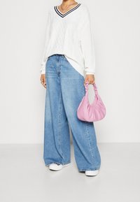 Vit stickad tröja med V-ringning, diamantmönster, oversize passform; ljusblå vida jeans; liten rosa läderväska med samlad handtag.