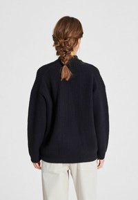 Juodas stripe pintas megztinis su laisvu siluetu, su nuleistais pečiais ir aukštu kaklu. Audinys yra minkštas, sukurtas patogumui.