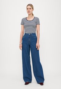 Striped navy and white fitted top paired with wide-leg, high-waisted blue denim jeans. Smooth texture with a relaxed silhouette and front pockets.