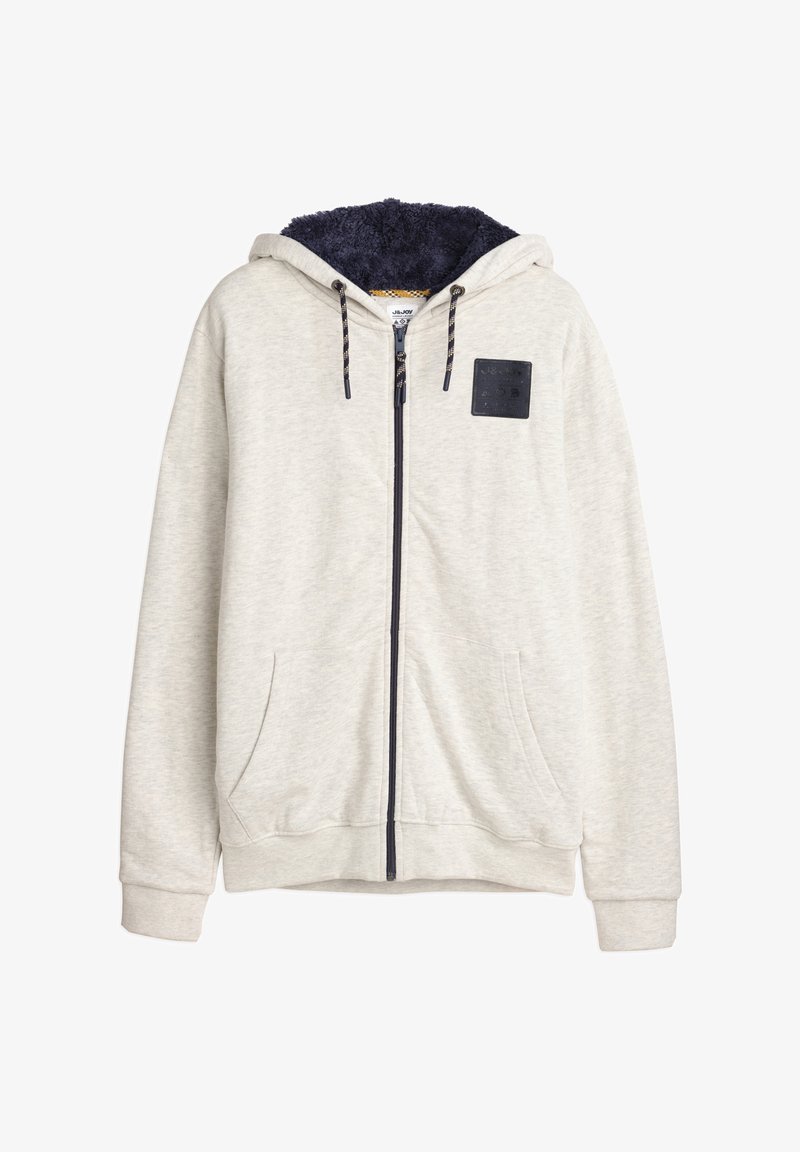 Haut de sweatshirt zippé gris clair avec une capuche en polaire bleu marine. Présente un patch noir texturé et des accents de cordon de serrage sur la capuche, ainsi que des poches avant.