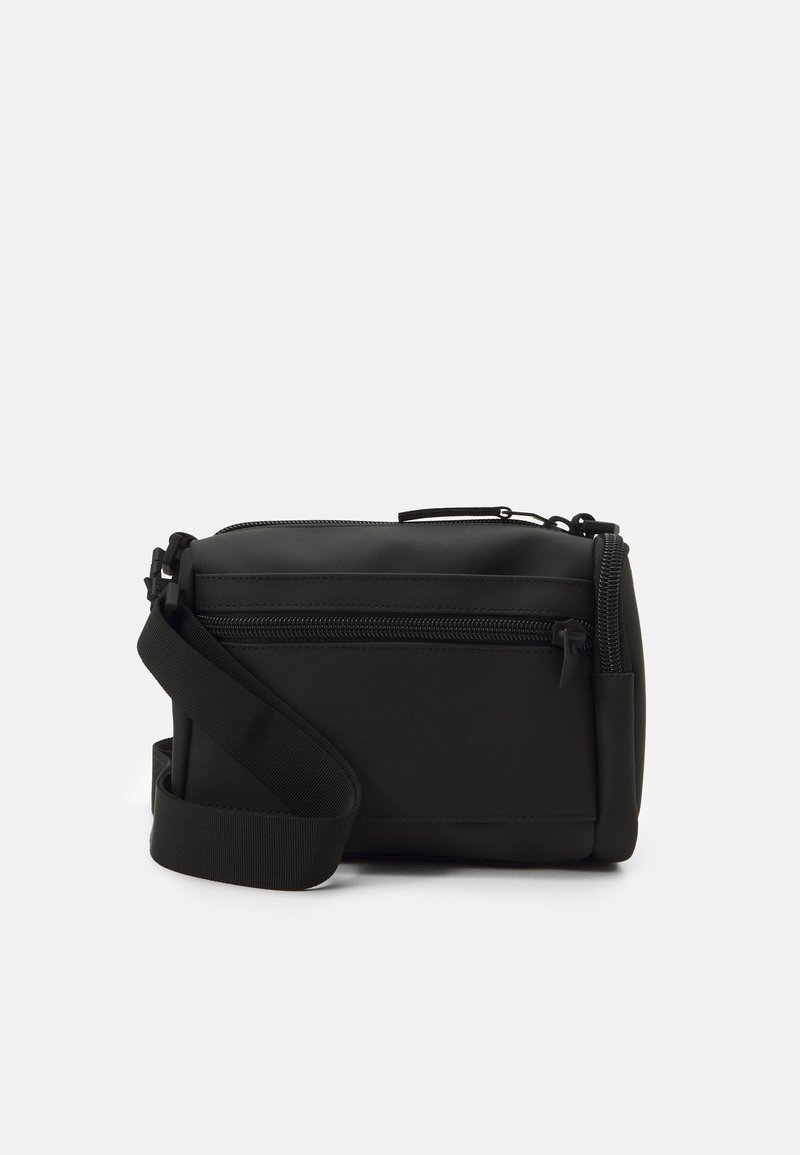 Sac noir rectangulaire en bandoulière en matière lisse, avec une fermeture éclair sur le dessus et une bandoulière ajustable. Design minimaliste sans motifs.