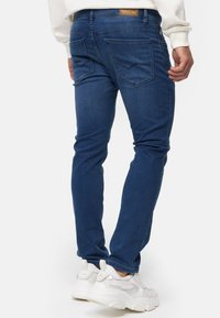 Mørkeblå denimjeans med smal passform, som har baklommer og en liten merkelapp. Kombinert med hvite tursko.