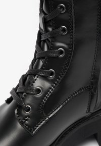 Botte en cuir noir à lacets avec surface texturée, bout rond, œillets renforcés et surpiqûres contrastées sur le côté.