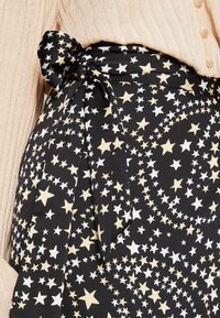 Jupe en tissu noir avec un motif d'étoiles blanches et dorées, dotée d'un détail de taille nouée et d'une texture douce, associée à un haut beige à côtes.