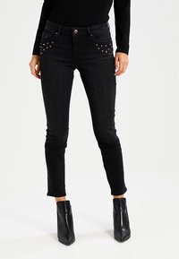 Svarta skinny jeans i denim med dekorativa nitar på framlappen, med en midja i medelhöjd och avsmalnande ben, i kombination med ankelstövlar.