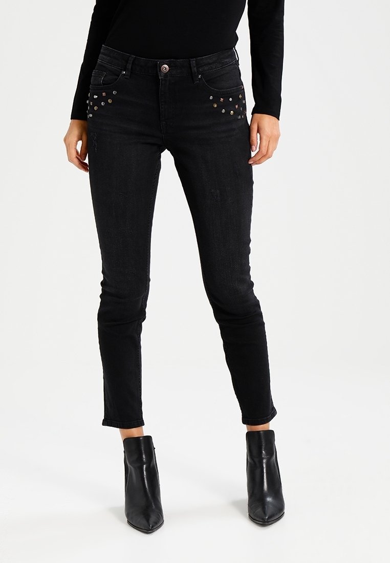 Svarta skinny jeans i denim med dekorativa nitar på framlappen, med en midja i medelhöjd och avsmalnande ben, i kombination med ankelstövlar.