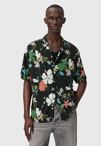 Czarna koszula z krótkim rękawem w kwiatowy wzór z żywymi zielonymi, białymi i czerwonymi kwiatami. Wykonana z lekkiego materiału o luźnym kroju.