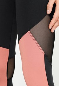 Leggings de alto rendimiento con tela negra y acentos de paneles en rosa y malla. Textura suave, diseño ajustado y con colores contrastantes.