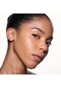 Vue de profil d'un visage avec une peau brun clair, une texture lisse, un petit nez, des lèvres pulpeuses et une boucle d'oreille en stud à l'oreille gauche.