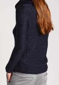 Dunkelblauer, gestrickter Pullover mit einem hohen, strukturierten Kragen und langen Ärmeln. Der Körper hat eine lockere Passform und gerippte Akzente an den Bündchen und dem Saum.
