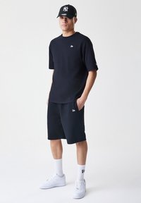 Marineblå kortermet T-skjorte og shorts-sett, laget av myk fabric, med logo og sidelommer, kombinert med hvite sneakers og sokker.