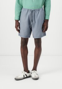 Pantalones cortos de algodón gris con cinturilla elástica y cordón de ajuste, que cuentan con bolsillos laterales y un corte relajado, combinados con zapatillas de caña baja.