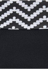 Zwarte stof met een gestructureerd wit zigzagpatroon aan de bovenkant, overgaand in een gladde zwarte stof eronder.