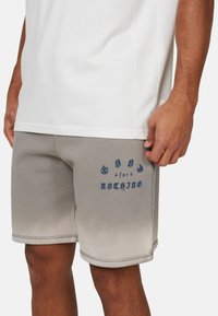 Shorts gris avec un design dégradé, texte graphique bleu "Good for Nothing", et une texture douce et lisse. Portés avec une chemise blanche.