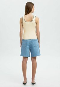 Beige soonik, millel on must äär, koos helesiniste teksashortsidega, mis on varustatud tagataskutega, vaadates seljatagant. Sile tekstuur.