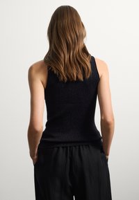 Top senza maniche nero a coste con un design aderente. Il materiale ha una leggera lucentezza, che completa dei pantaloni neri larghi. Texture liscia.