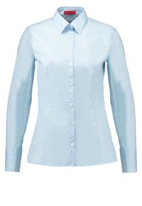 Chemise cintrée bleu clair à manches longues, à boutons, avec col pointu et boutons blancs, avec une étiquette rouge à l'intérieur du col.