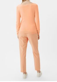 Pull en maille pêche avec un col large, associé à un pantalon pêche. Le mannequin porte des baskets blanches. Texture douce et design épuré.