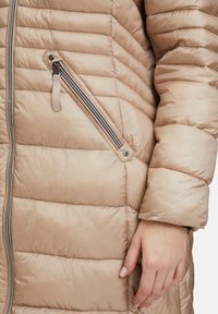Hellbeige, gestepptes Daunenjacke mit diagonalen Nähten, seitlichem Reißverschlussfach und metallischem Reißverschlussanwender. Weiche, glatte Textur.