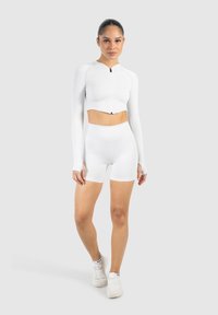 Chaqueta atlética blanca de cropped con cremallera y pantalones cortos de tiro alto, ambos en textura acanalada, combinados con zapatillas blancas.