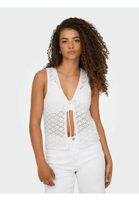 Witte gehaakte vesttop met V-hals, striksluiting aan de voorkant en geometrische patronen. Gecombineerd met witte broek met een slim fit.