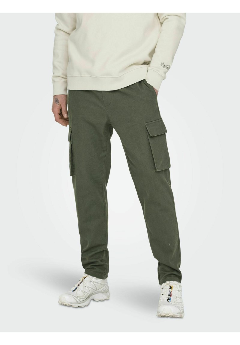 Cargo-Hosen aus olivgrünem Stoff mit seitlichen Taschen, geradem Schnitt und elastischen Bündchen, kombiniert mit weißen Sneakern.