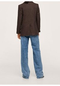 Bruine blazer met textuur en een enkele split, gecombineerd met loszittende lichtblauwe spijkerbroeken. Gezien van achteren, met knoopdetails.