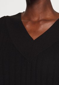 Top a coste nera con scollatura a V, caratterizzato da una superficie tessurizzata e un design aderente, evidenziando una finitura liscia ed uniforme.