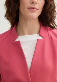Blazer rose texturé avec un col cranté, porté sur une chemise blanche. Mettez l'accent sur les détails de conception et de matériau.