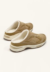 Brune ruskind slip-on-træsko med et blødt hvidt pelsenindlæg, der har buede designaccent og en tekstureret gummisål for greb.