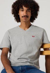 Siva kratka majica s kratkimi rokavi in V-izrezom, s malim rdečim logotipom Levi's na prsih, izdelana iz mehkega, teksturiranega materiala.