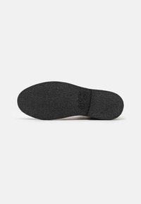 Black rubber shoe sole with a textured surface and subtle branding. Rounded toe and contoured heel for stability. Flat profile design.