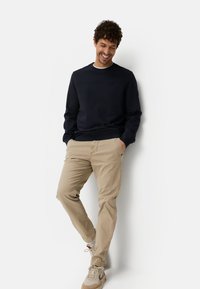Marineblauer Sweatshirt mit Rundhalsausschnitt und Nahtdetail, kombiniert mit beigen Chinos und beigen Sportschuhen. Legerer, lockerer Schnitt mit langen Ärmeln.