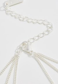 Silver kedja med ett spänne och flera sammanflätade trådar, som visar en slät yta och en glänsande finish.