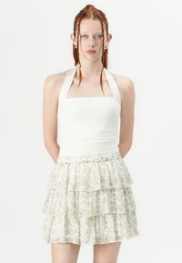 Top halter bianco con scollo quadrato abbinato a una mini gonna a strati e volant in tessuto trasparente con un motivo floreale nei toni del rosa chiaro e del verde.
