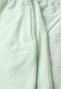 Jasnozielone dresy o miękkiej teksturze, z wytłoczonym logo "SUPERDRY" na udzie oraz boczną kieszenią dla wygody.