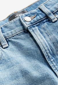 Ljusblå denimjeans med knappstängning i midjan, med fickor och kontrasterande sömmar. Mjuk textur med ett slitet utseende.