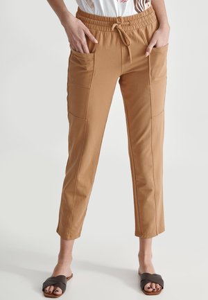 Tan, cropped pants made of soft, stretchy material. Features an elastic waistband with a drawstring and two side pockets.
