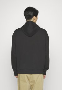 Black hoodie with a large hood, ribbed cuffs, and hem. Made from soft fabric, features a relaxed fit and is styled without front detailing.